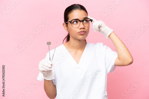 Dentist Colombian woman isolated on pink background having doubts and thinking