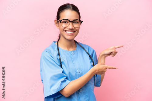 Young nurse Colombian woman isolated on pink background pointing finger to the side and presenting a product photo