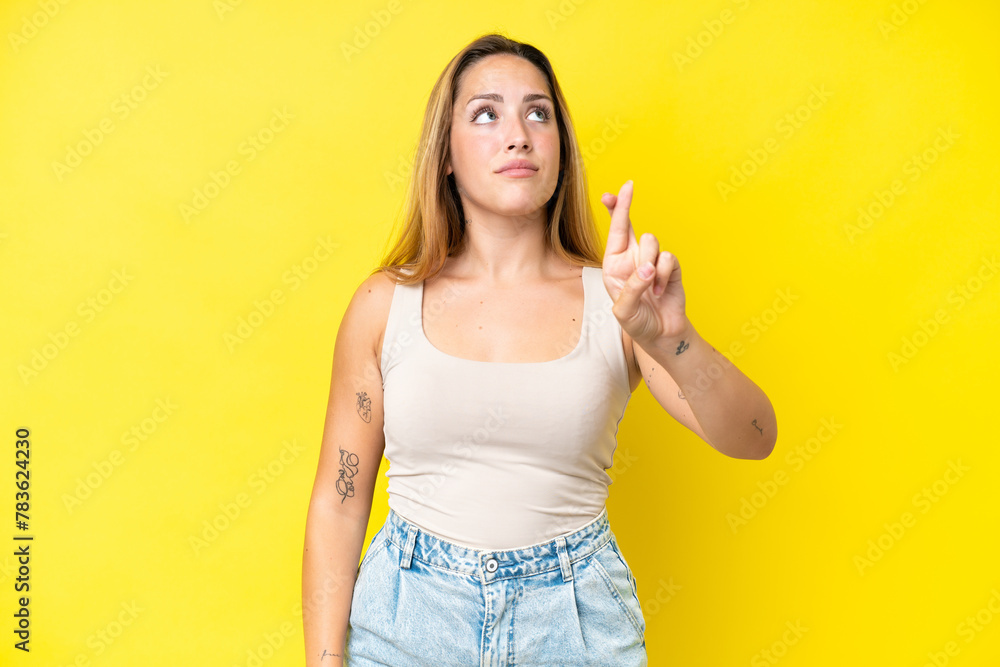 Young caucasian woman isolated on yellow background with fingers crossing and wishing the best Young caucasian woman isolated on yellow background with fingers crossing and wishing the best