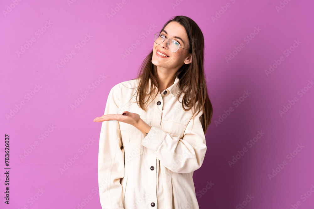 Young woman over isolated purple background presenting an idea while looking smiling towards Young woman over isolated purple background presenting an idea while looking smiling towards