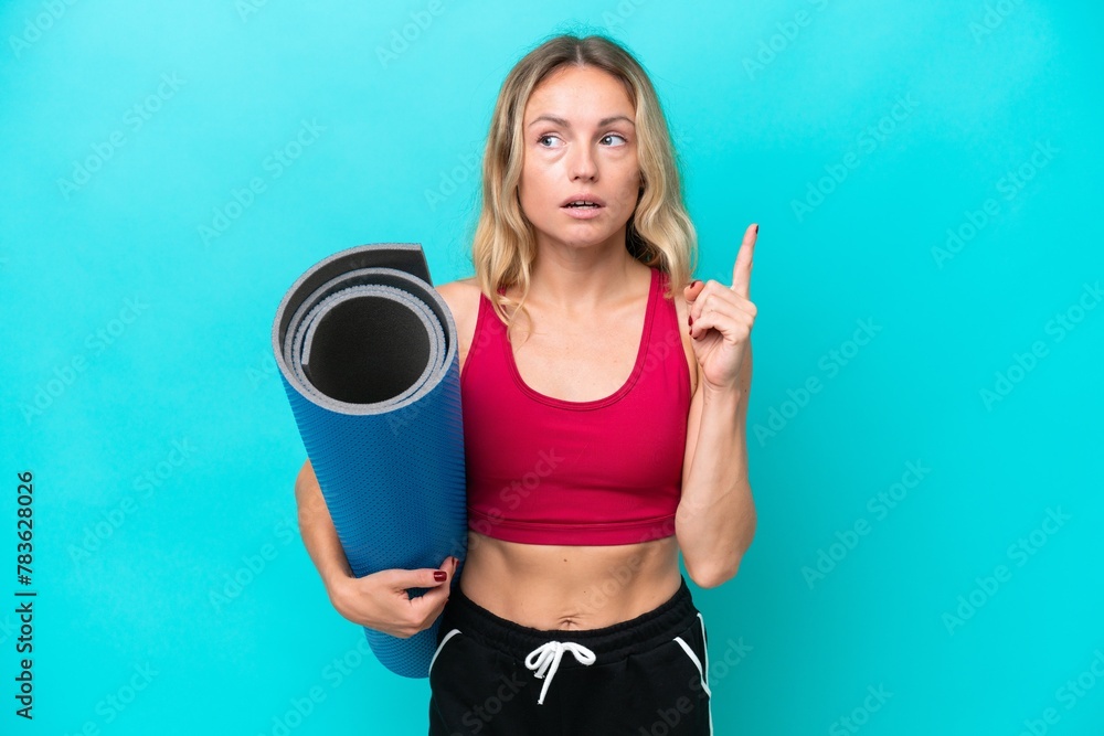 Young sport Russian woman going to yoga classes while holding a mat isolated on blue background thinking an idea pointing the finger up Young sport Russian woman going to yoga classes while holding a mat isolated on blue background thinking an idea pointing the finger up