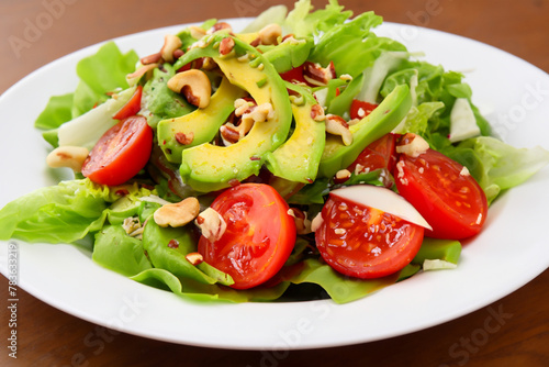 light salad. on a wooden table there is a white plate with avocado tomato and nut salad, top view, healthy concept