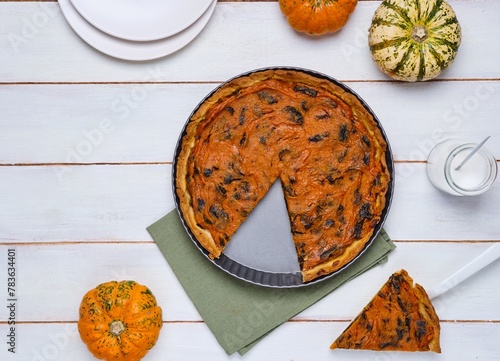 Round tart with pumpkin and prunes in the form for baking on a light derving background. Pumpkin recipes. French cuisine. photo