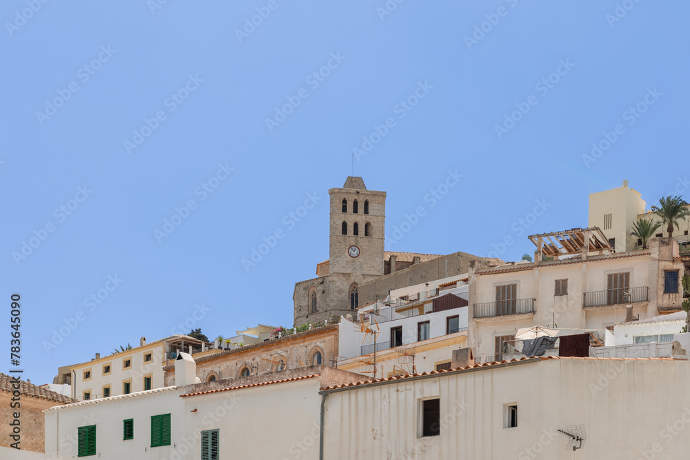 The tower of Eivissa town castle in Ibiza, Spain, emerges above the dense old town architecture, framed by the clear Mediterranean sky