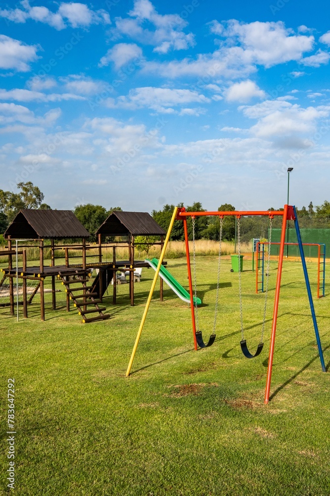 Vertical shot of a playground with colorful swings and wooden gazebos on a sunny day Vertical shot of a playground with colorful swings and wooden gazebos on a sunny day