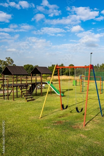 Vertical shot of a playground with colorful swings and wooden gazebos on a sunny day