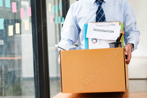 Man leaves office holding a box with personal items, including resignation letter.