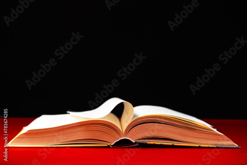 Pages of a thick book are turned on a red and black background, space for text.