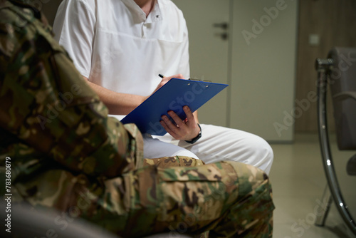 Medical professional writing on clipboard health complaints of serviceman
