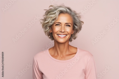 A woman with a short, curly gray hair is smiling and wearing a pink shirt