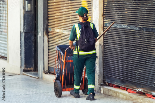 Female cleaner in a green uniform with a garbage container in Latin America. photo