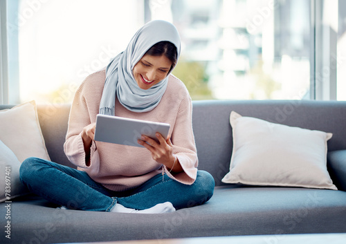 Smile, reading and muslim woman with tablet on sofa for online ebook in living room at home. Happy, relax and islamic female person enjoying internet story, novel or literature on digital technology