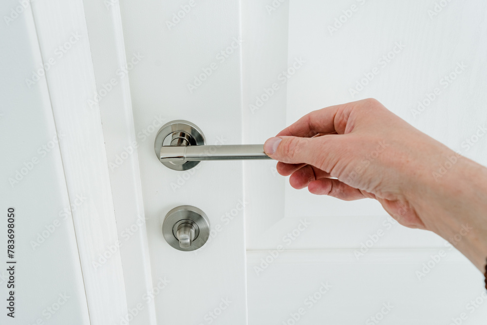 Fototapeta premium Hand holding door handle on white background, man opening snow-white door to room.