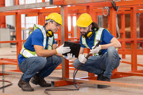 Caucasian iron welding workers with tablet in front of the red steel structure photo