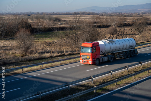 A red tanker drives along the highway through rural landscapes. The tank has a chrome-plated round trailer for transporting liquid substances, fuel, gasoline, diesel, dangerous substances.
