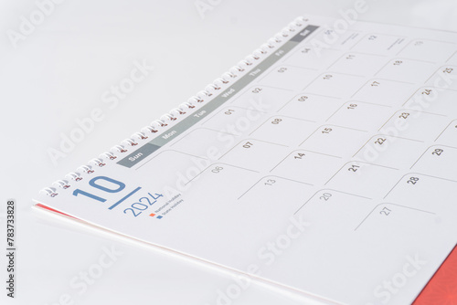 A spiral bound paper calendar. October page of 2024 calendar displayed on white background, side view and selective focus shot. 