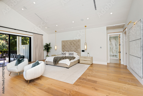 this bedroom has white walls and wood flooring, a bed with two armchairs