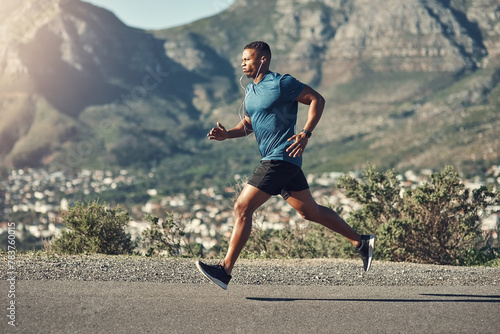 Black man, running and outdoor with workout, exercise and motivation or training for future sports competition. Athlete, jog and road for fitness, health and performance with stopwatch or music