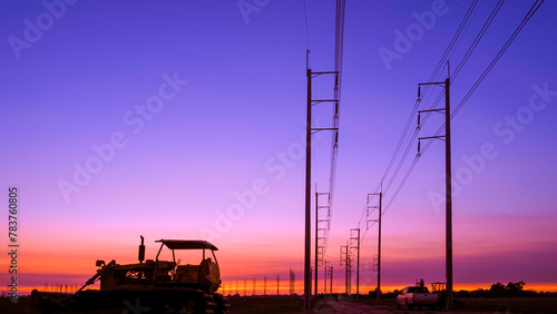 Silhouette of bulldozer tractor with row of electric poles in countryside area against colorful twilight sky background
