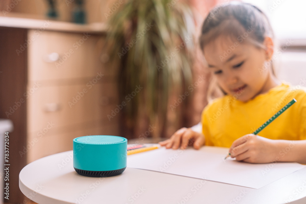 Child draws at the table and talks to a blue smart speaker. Child draws at the table and talks to a blue smart speaker.
