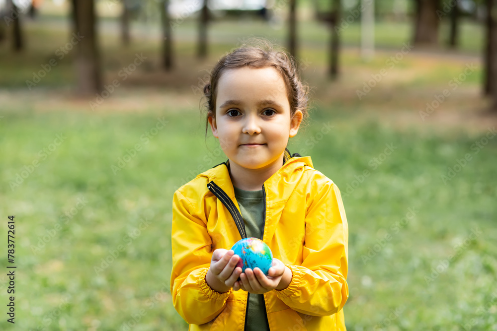 Child kid girl in a yellow raincoat holding globe in a hands outdoor in park or forest. World Earth Day concept. Green Energy, renewable and sustainable resources. Protecting and save planet. Child kid girl in a yellow raincoat holding globe in a hands outdoor in park or forest. World Earth Day concept. Green Energy, renewable and sustainable resources. Protecting and save planet.