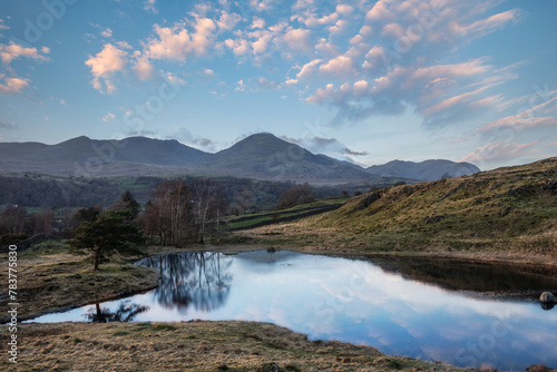 Stunning sunset landscape image of Kelly Hall Tarn in Lake District with Old Man of Coniston in background