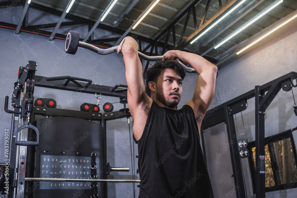 A fit asian man does a set of EZ bar standing french presses. Training triceps and upper arms at the gym. A fit asian man does a set of EZ bar standing french presses. Training triceps and upper arms at the gym.