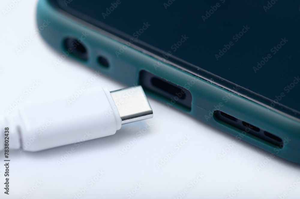 Zbliżenie na końcówkę od ładowarki wpięta w rozładowany smartfon na białym tle Zbliżenie na końcówkę od ładowarki wpięta w rozładowany smartfon na białym tle