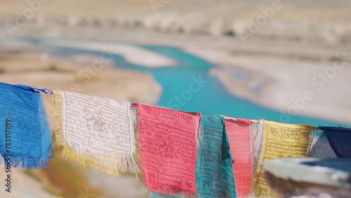 Slow motion shot of Buddhist Prayer flags waving in front of the blue coloured Zanskar river as seen from Padum village in Zanskar Valley, Ladakh, India. Prayer flags wave in front of river in India. photo