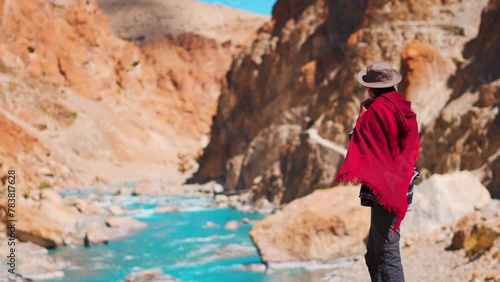 Rear view shot of an Indian man wearing hat and shawl looking at the blue Tsarap Chu river on the way towards Phugtal Monastery in remote area of Zanskar Valley in Ladakh, India. Tourist in Himalayas. photo