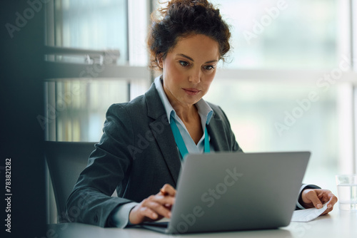 Female CEO using laptop while working on business reports in office.