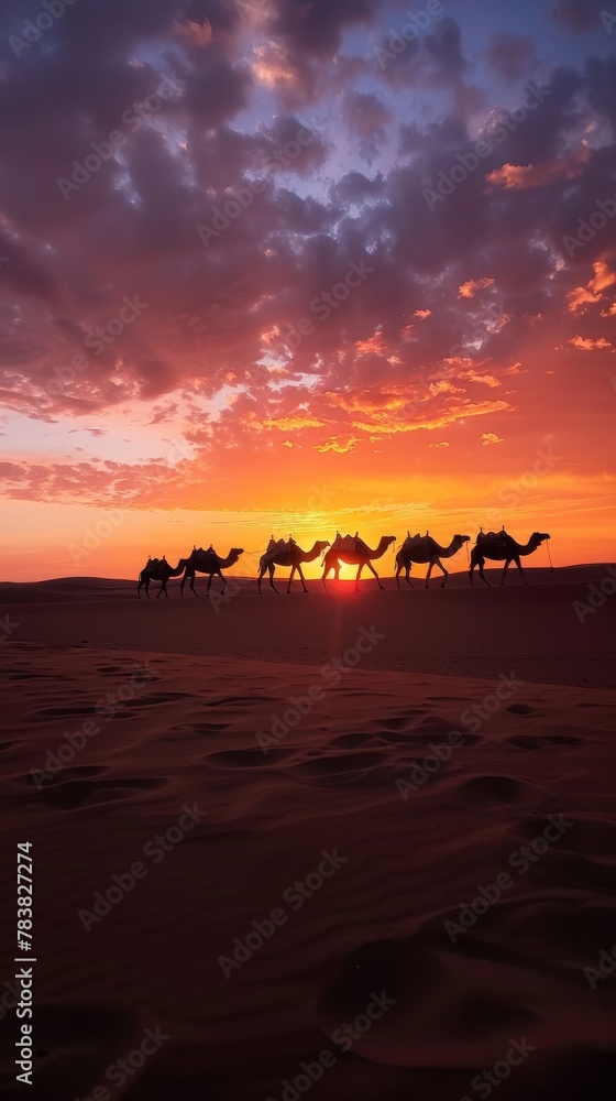 Silhouette of a caravan of camels crossing a serene desert at sunset, under a fiery sky.