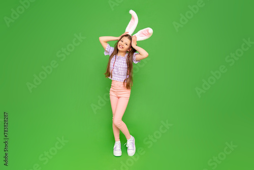 A charming little girl dressed up as an Easter bunny is enjoying the Easter holiday. A full-length child with rabbit ears on his head. Green isolated background. Copy space.