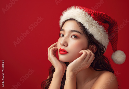 beautiful woman in santa hat with hands on chin looking left against a red background