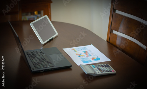 The laptop, tablet and calculator were on the table, with business graphs laying next to it.