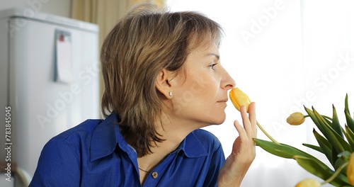 Middle-aged woman inhales yellow tulip scent. Flower fragrance, natural aromatherapy moment, Gen X. Flowers essence, peaceful woman. Flowers allure, tranquil experience, mature lady delight.