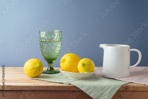 Summer composition with lemons and white jug on kitchen wooden table