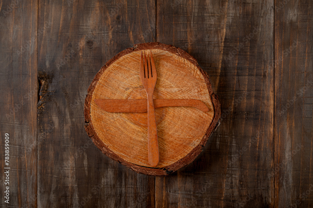 Tree trunk slice with set of wooden fork and knife imitating a clock on dark wood background