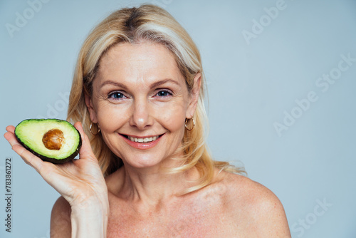 Cincematic image of a beautiful senior woman posing on a beauty photo session. Middle aged woman holding an half avocado. Concept about body positivity, self esteem, and body acceptance