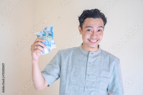 Moslem Asian man happy, smiling when got THR money Ramadan celebration. The photo is suitable to use for Ramadhan poster and Muslim content media.