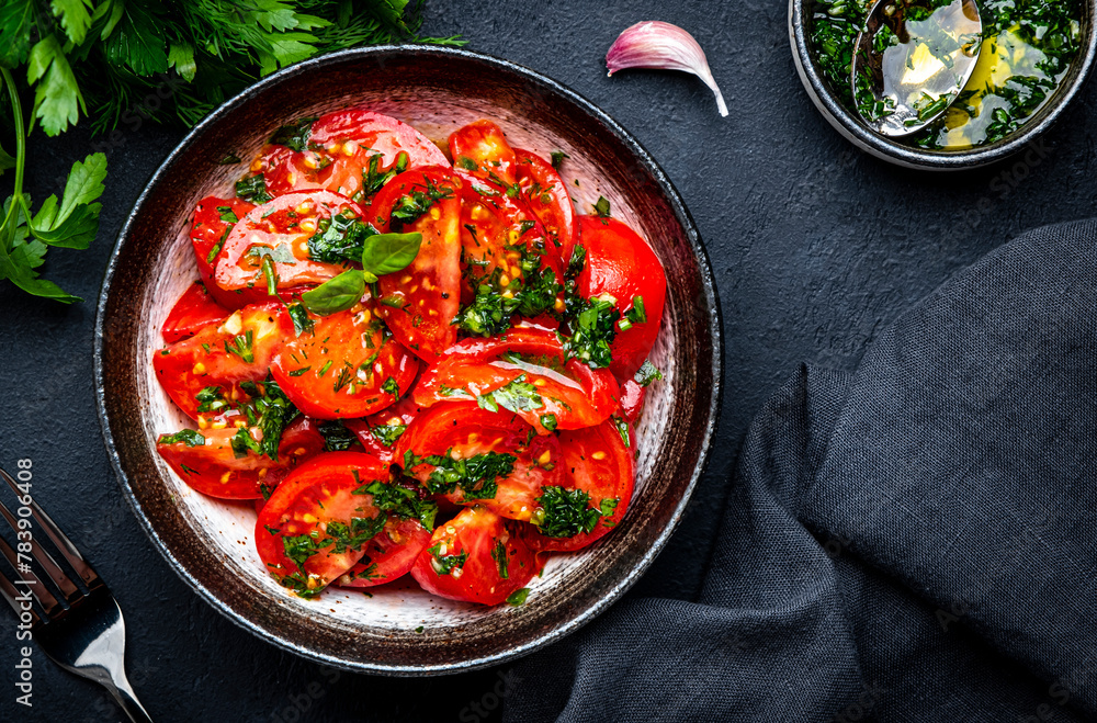 Simple summer juicy tomato salad with parsley, dill, garlic and olive oil dressing, black stone table background, top view Simple summer juicy tomato salad with parsley, dill, garlic and olive oil dressing, black stone table background, top view