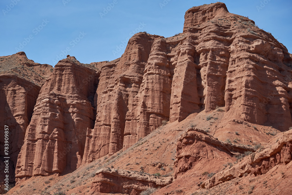 Fototapeta premium Sheer cliffs subject to erosion, red rocks of the Konorchek canyon, travel destination, famous landmark Kyrgyzstan, Central Asia. Rock formation, natural landscape, hiking trekking area, sandstone