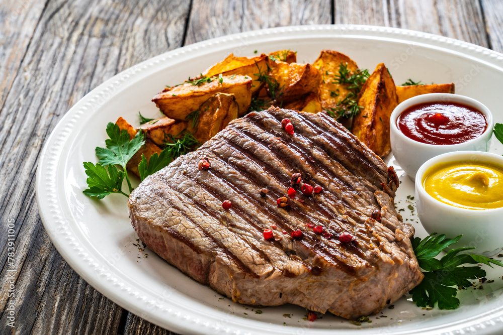 Grilled beef sirloin steak with baked potatoes on wooden table
