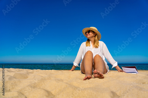 Mid-adult woman sitting on beach reading book 