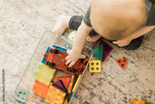 Baby sitting playing with magnetic tiles in a clear bin