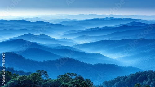   A panorama of mountain ranges from a hilltop, bathed in sky's blue hues Trees populate the foreground