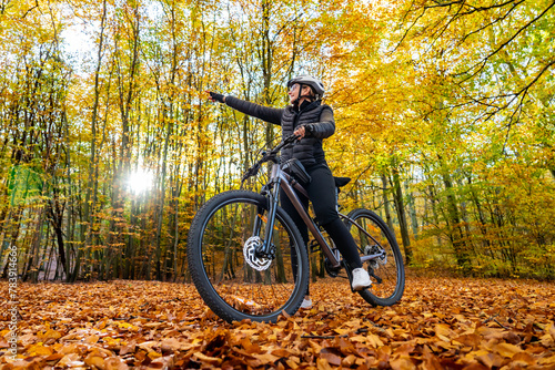 Woman riding bicycle in city forest in autumn scenery
