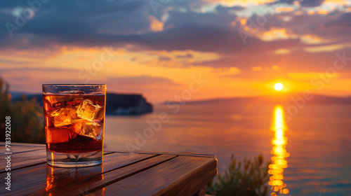 Close up portrait of glass of alcohol with ice cubes on wooden table top at beach, beautiful evening sunset with tropical beach and sky