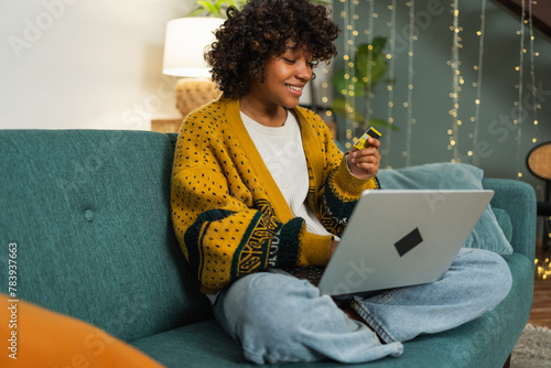 African American woman using laptop shopping online paying with gold credit card. Girl sitting at home buying on Internet enter credit card details. Online shopping ecommerce delivery service