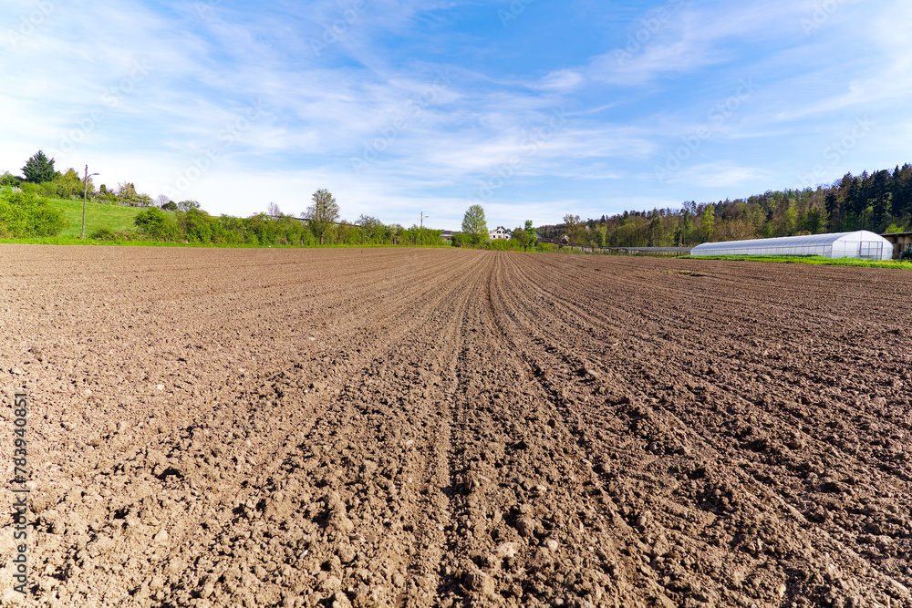 Diminishing view of freshly ploughed agriculture field at farm with white greenhouse in the background on a sunny spring day. Photo taken April 13th, 2024, Zurich, Switzerland. Diminishing view of freshly ploughed agriculture field at farm with white greenhouse in the background on a sunny spring day. Photo taken April 13th, 2024, Zurich, Switzerland.